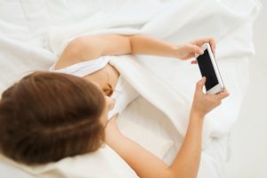 child, technology and internet concept - little girl lying in bed with smartphone at home
