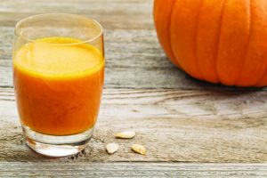 a glass of fresh pumpkin juice on a rustic wooden table with pumpkin and seeds