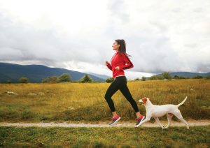 Young woman jogging through the countryside with her pet dog. Taken on a rainy day, under the cloudy sky.